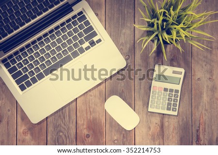 Top view working desk with laptop computer, calculator and plant pot. Wooden table background with copy space in vintage toned.