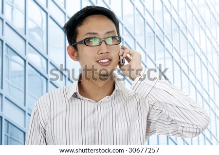 Asian businessman laughing while talking on his cellular in front modern building.