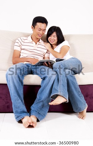 Reading together. Asian couples sitting on sofa sharing a book.