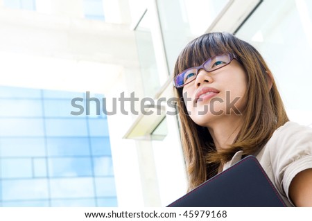Business Outlook. A young Asian woman looking far away to bright light in front of a modern office building, with diary on hand.