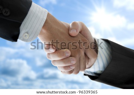 Businessmen shaking hands over blue sky, low angle view.