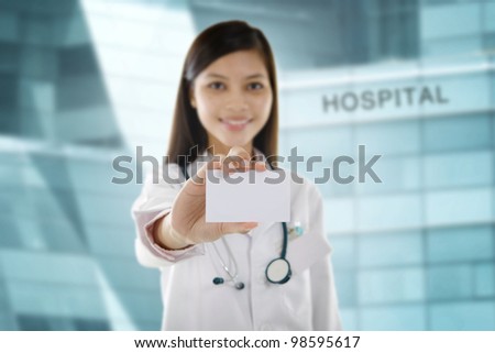 Asian mixed race female doctor holding business card in front hospital building