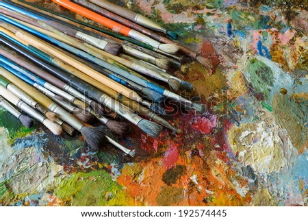 art brushes lie on a colourful oil palette