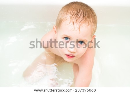 four year old boy sitting in water in the bathroom and looking at the camera. The boy\'s face close up