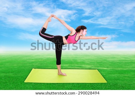 Young woman doing yoga exercise with yoga mat on green grass and blue sky