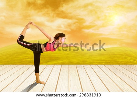 Young woman doing yoga exercise on wood floor with field at sunset