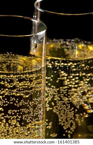 a pair of flutes of champagne tilted with golden bubbles on black background and space for text