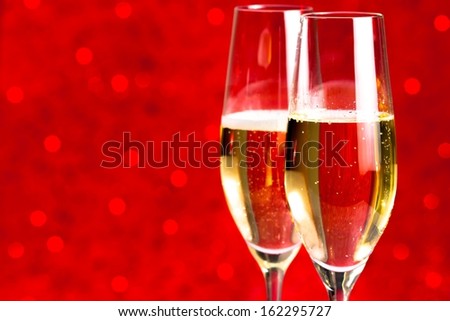 a pair of flutes of champagne on red bokeh background with space for text