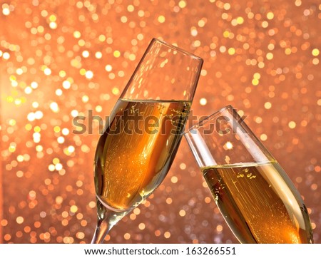 pair of a champagne flutes with gold bubbles make cheers on light bokeh background