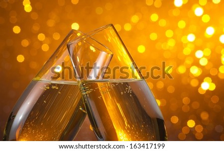 two champagne flutes with gold bubbles make cheers on dark light bokeh background with space for text