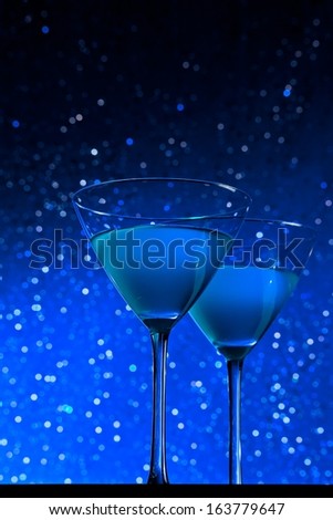 a pair of glasses of blue cocktail on dark blue tint light bokeh background