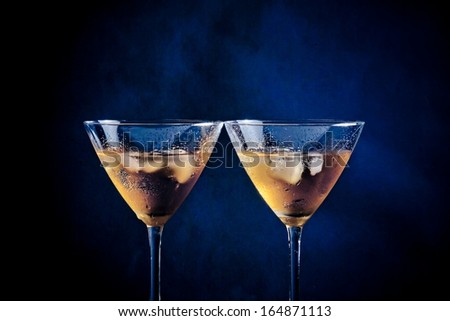 a pair of glasses of  fresh cocktail with ice on blue tint light background on bar table