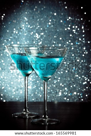 Glasses Of Fresh Blue Cocktail With Ice On Blue Tint Light Bokeh Background On Bar Table