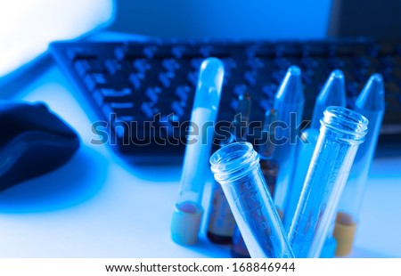 test tubes in laboratory on table near computer keyboard and mouse on table and blue light tint background