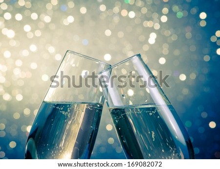 Champagne Flutes With Golden Bubbles Make Cheers On Blue Light Bokeh Background With Space For Text