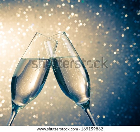 Champagne Flutes With Golden Bubbles Make Cheers On Blue Light Bokeh Background With Space For Text