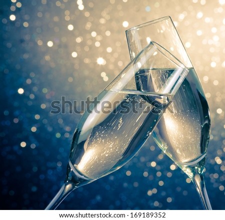 two champagne flutes with golden bubbles make cheers on blue light bokeh background with space for text