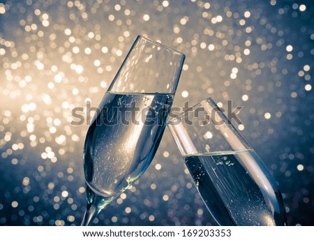 a pair of champagne flutes with golden bubbles make cheers on blue light bokeh background with space for text