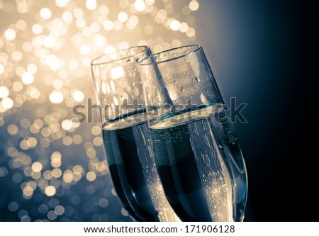 detail of champagne flutes with golden bubbles on dark blue light bokeh background with space for text