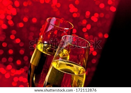 champagne flutes with golden bubbles on dark red light bokeh background with space for text