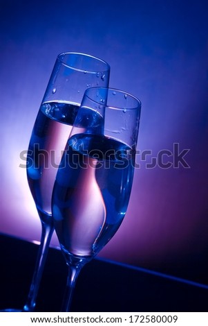 champagne flutes on bar table on dark blue and violet light background with space for text