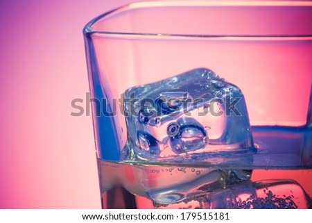glass of a drink with ice on disco violet light on white table with space for text