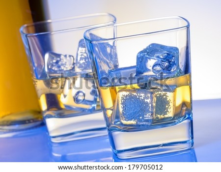 two glasses of whiskey with ice on blue light on white bar table