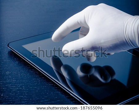 hand in medical glove touching modern digital tablet pc on wood table. Concept of medical or research theme