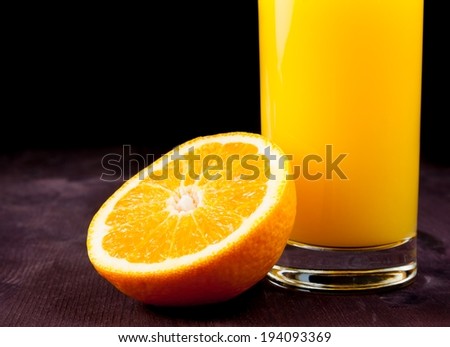 detail of full glass of orange juice near half orange on wood table