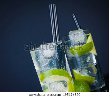 two glasses with cocktail and ice with lime slice on dark blue background, disco club atmosphere