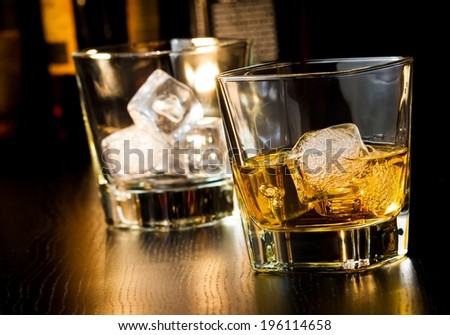 whiskey glass with ice in front of empty whiskey glass on wood table