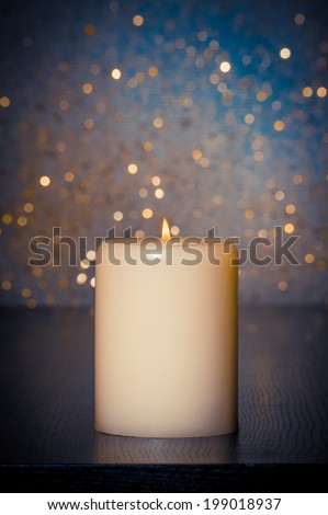 candle with flame on wood table and blue bokeh background and space for text