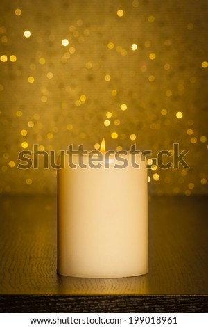 candle with flame on wood table and gold bokeh background and space for text