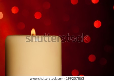 half candle with flame on wood table and red bokeh background and space for text