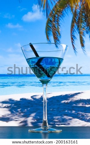 blue cocktail on beach and wood table, blue sea and sky background