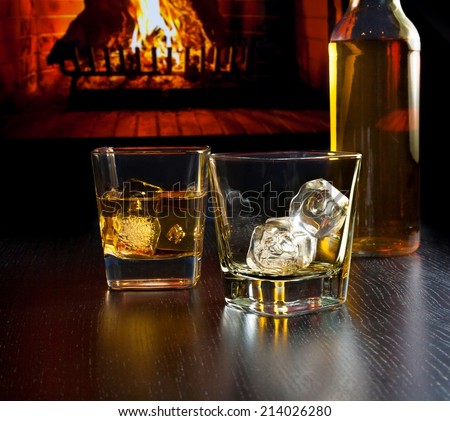 glasses of whiskey with ice cubes near whiskey bottle in front of the fireplace at night