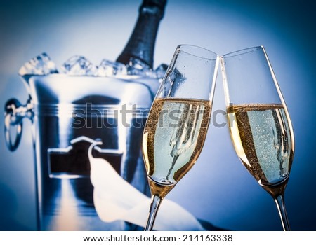 champagne flutes with golden bubbles make cheers in front of champagne bottle in bucket background