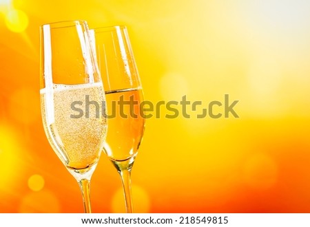 champagne flutes with golden bubbles on golden light background with space for text