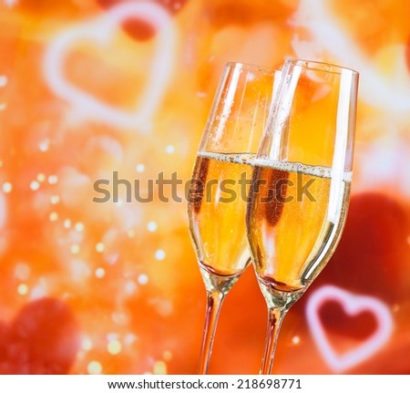 a pair of champagne flutes with golden bubbles on blur decorative hearts background love concept