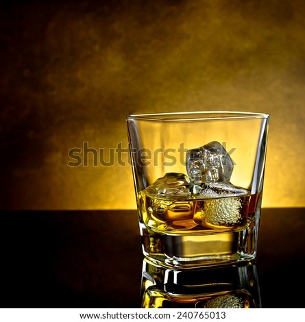 whiskey glass with ice and warm light on black table with reflection and warm atmosphere