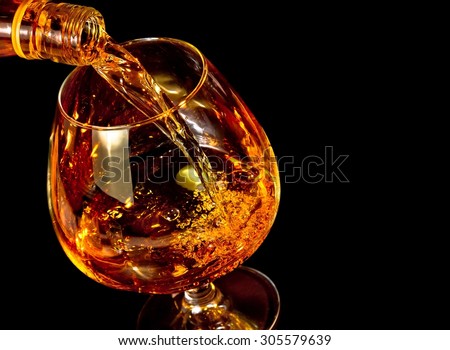 barman pouring snifter of brandy in elegant typical cognac glass on black background with space for text