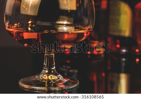 snifter of brandy in elegant typical cognac glass  in front of bottles in background, warm atmosphere