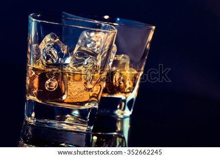 two glasses of whiskey with ice cubes on black background with light tint blue and reflection, time of relax with whisky