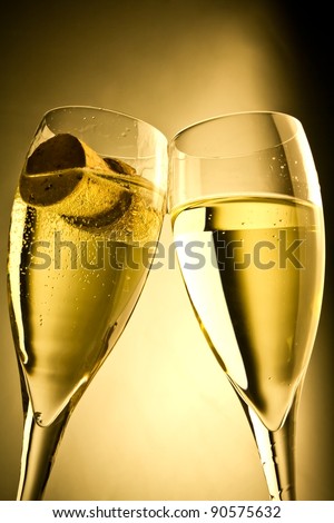 close up a pair of champagne flutes with bottle cap against a golden background