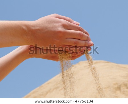 hands dropping sand against blue sky