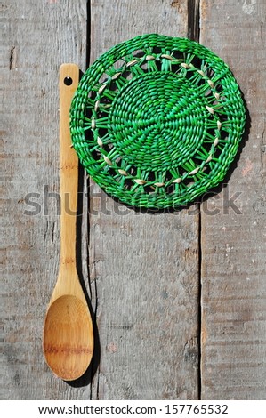 Wooden kitchen spoon and green wicker napkin on a wooden counter with copyspace