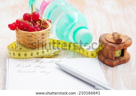 Planning of a diet. A notebook with inscription - My Diet, a measuring tape, water and red currant