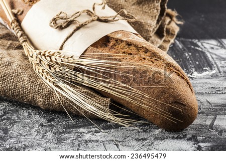 black long loaf with ears of wheat on a dark background with flour