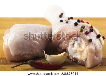 marinated chicken legs on a wooden board with spices, white background