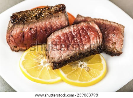 Sliced grilled meat with slices of lemon on a white plate
